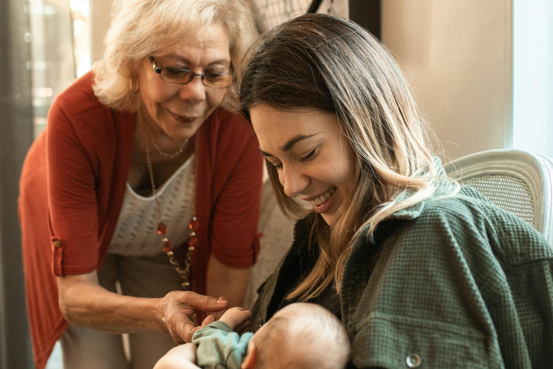 Grandmother gently touching a newborn held by the mother.