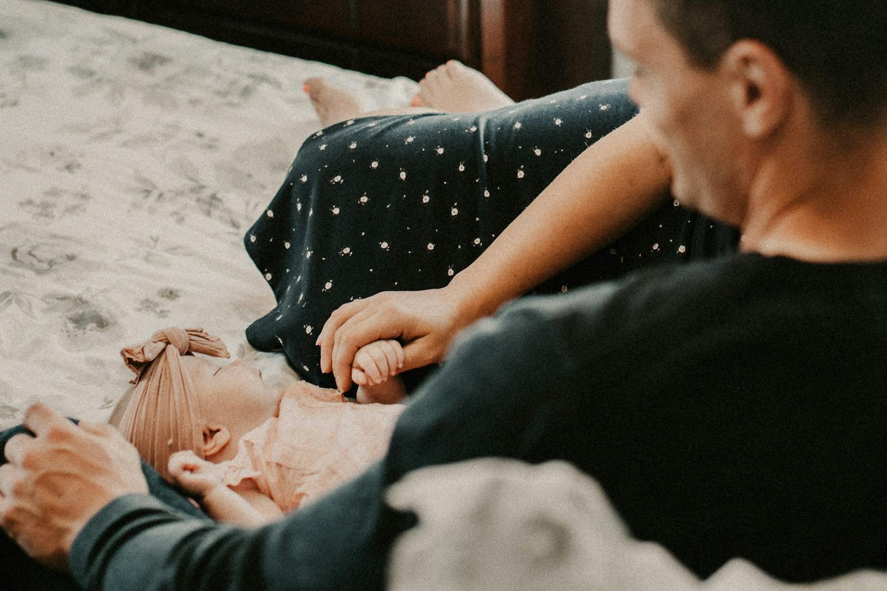 Parents sitting on a bed while bonding with their newborn baby.