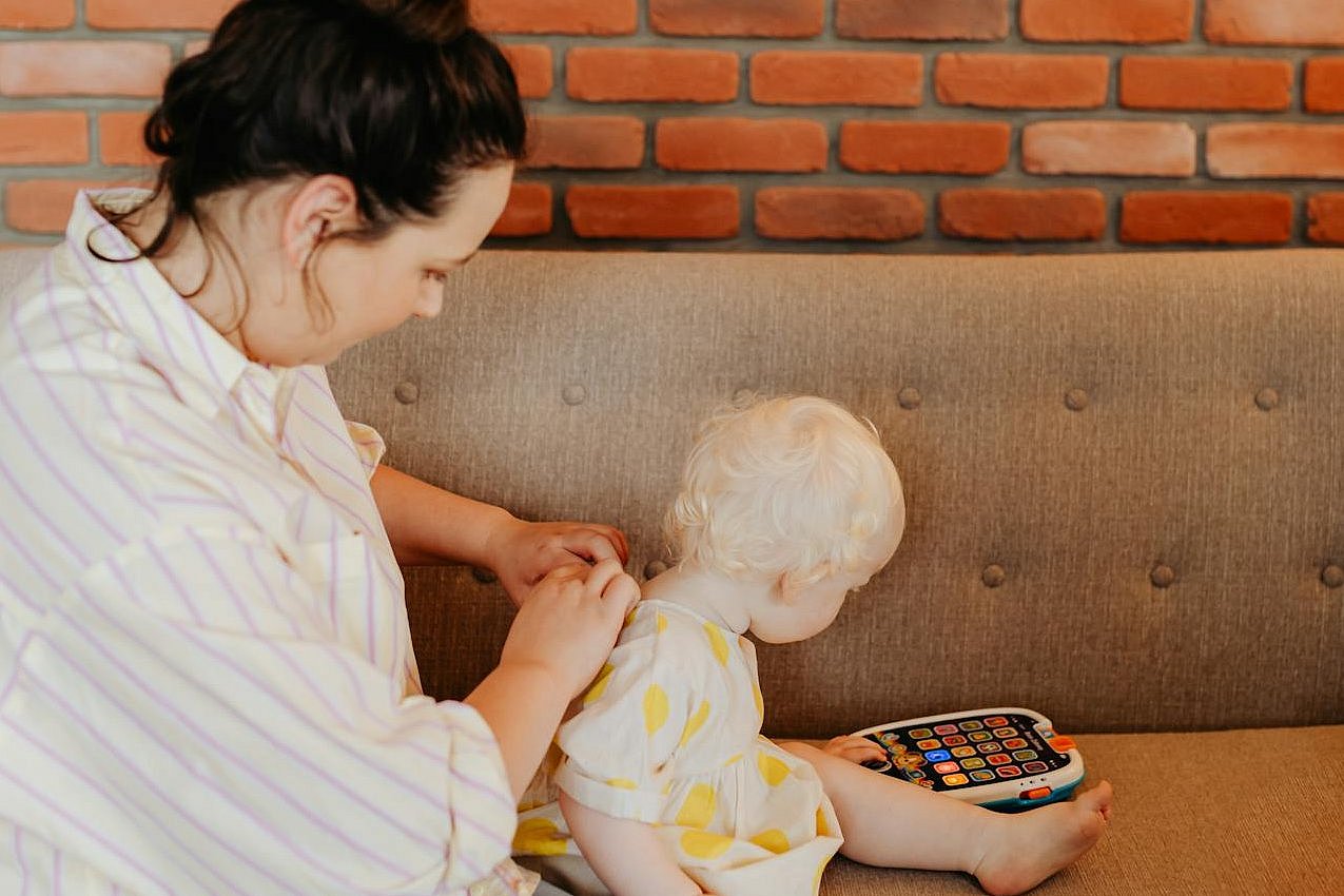 Mother dressing her child who’s playing with a toy.