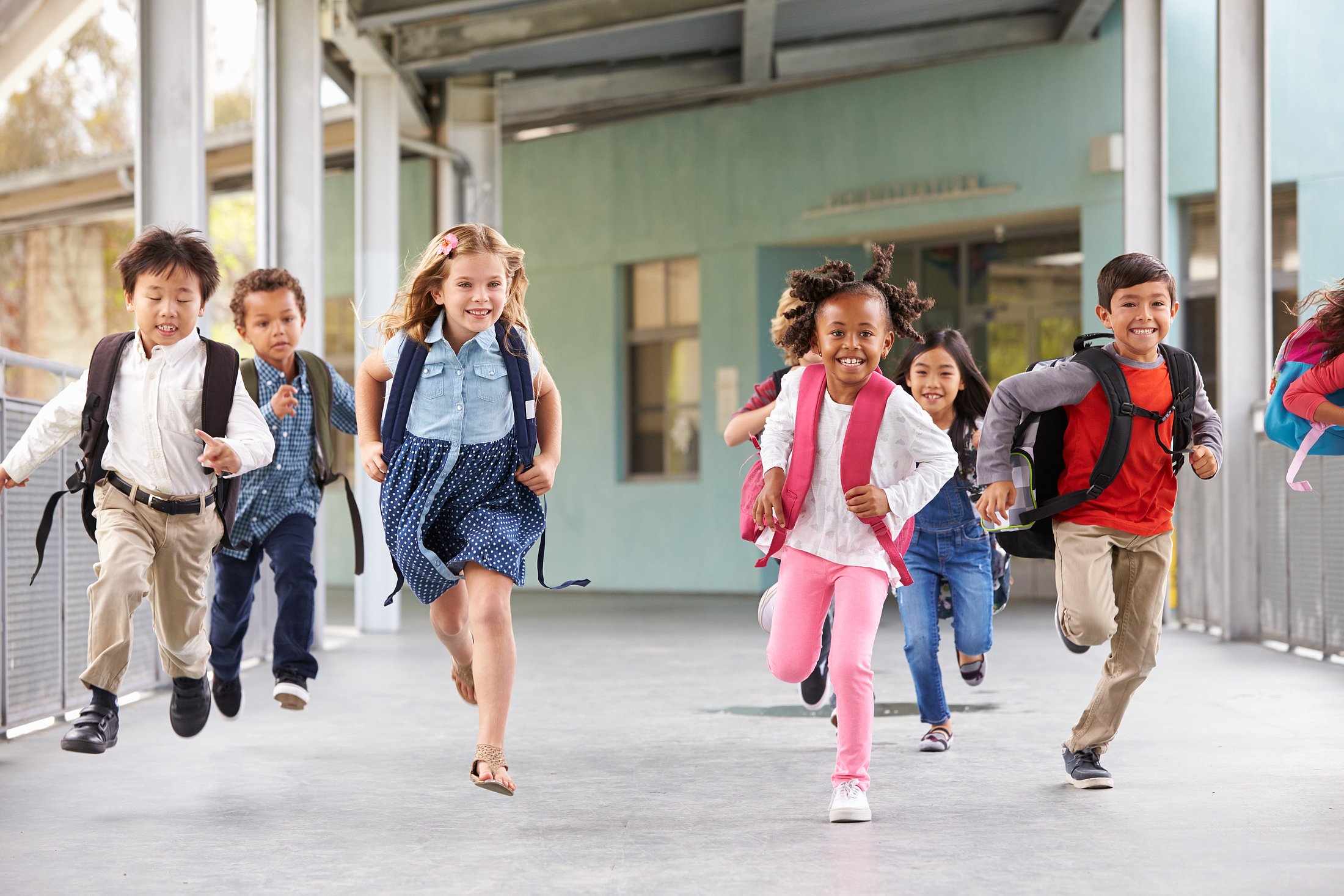 A group of young children running with backpacks at school.