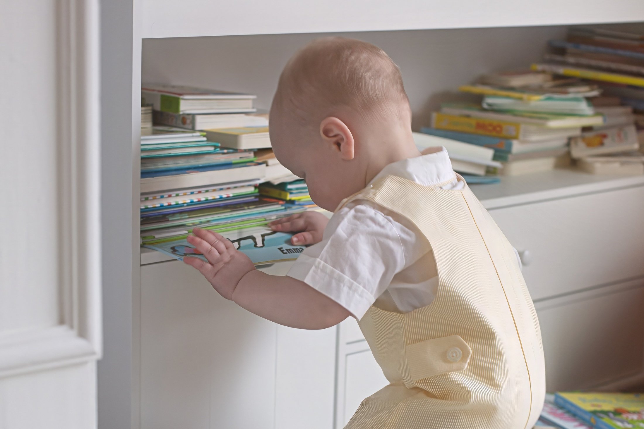 Baby exploring books on a shelf, surrounded by colourful books.