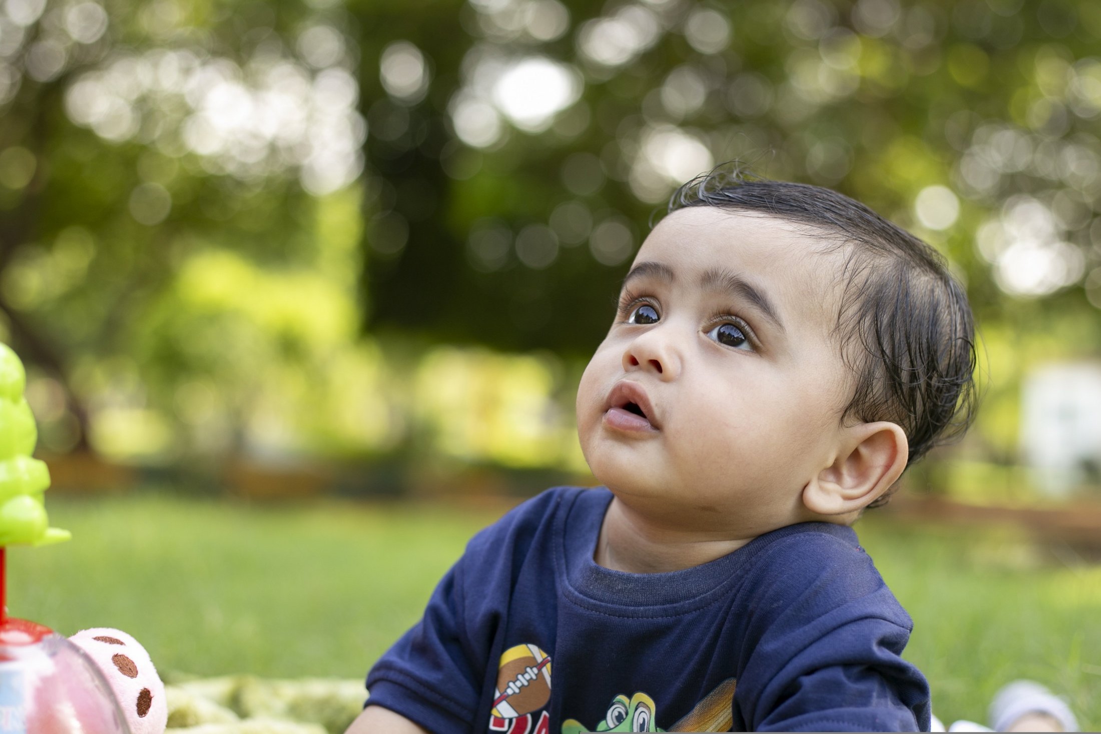 A baby looking up while playing on a blanket outdoors.