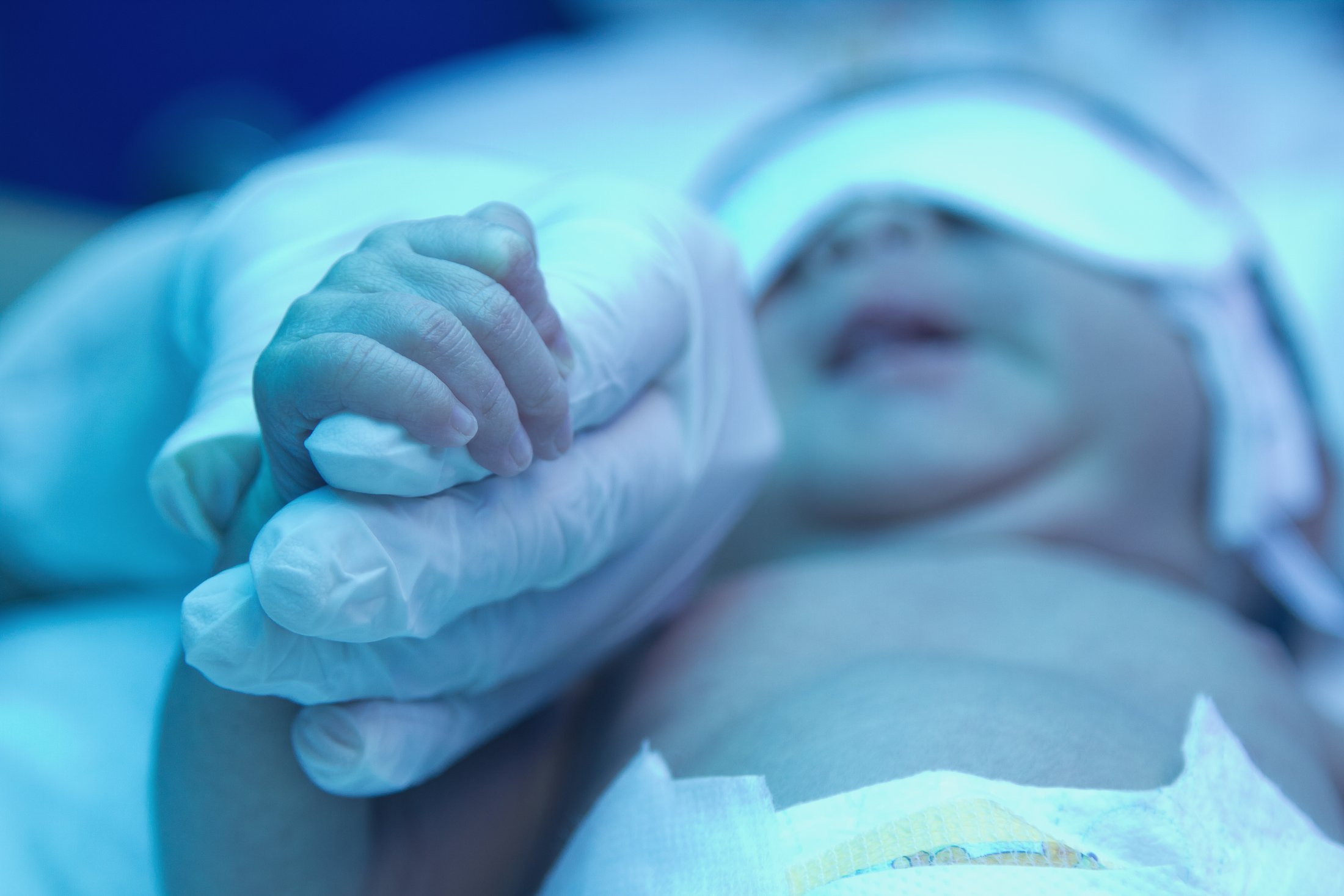 Nurse holding the hand of a premature baby in neonatal care.