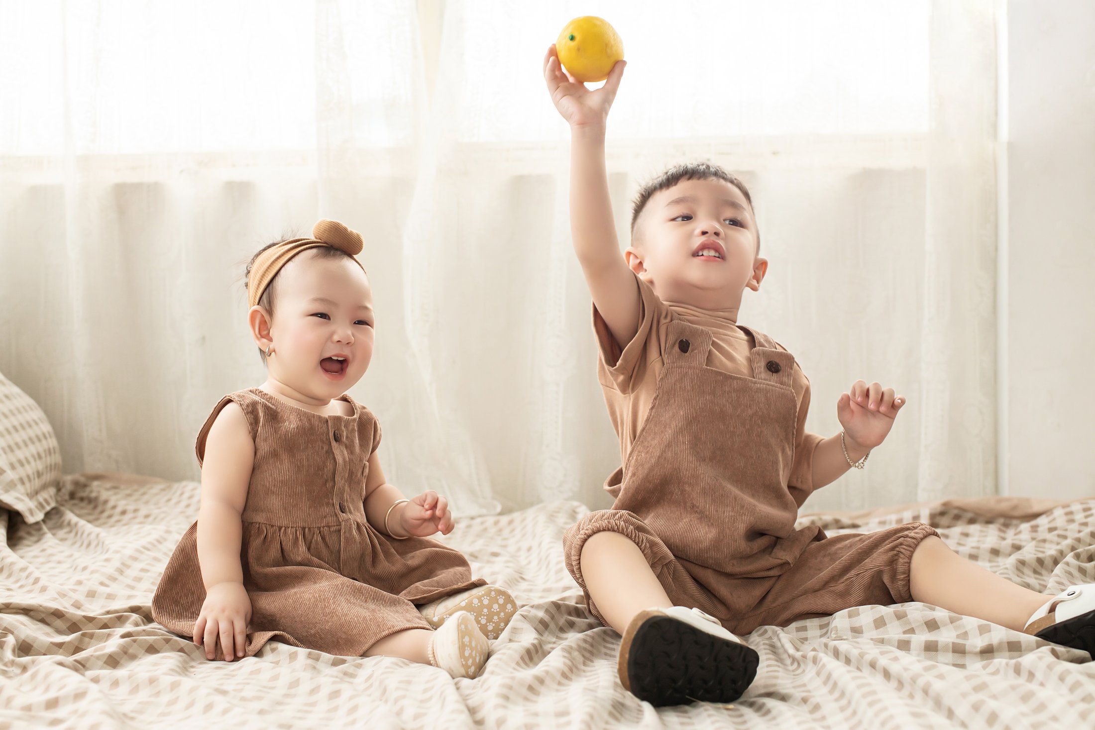 A toddler and baby sister laughing together while playing indoors.