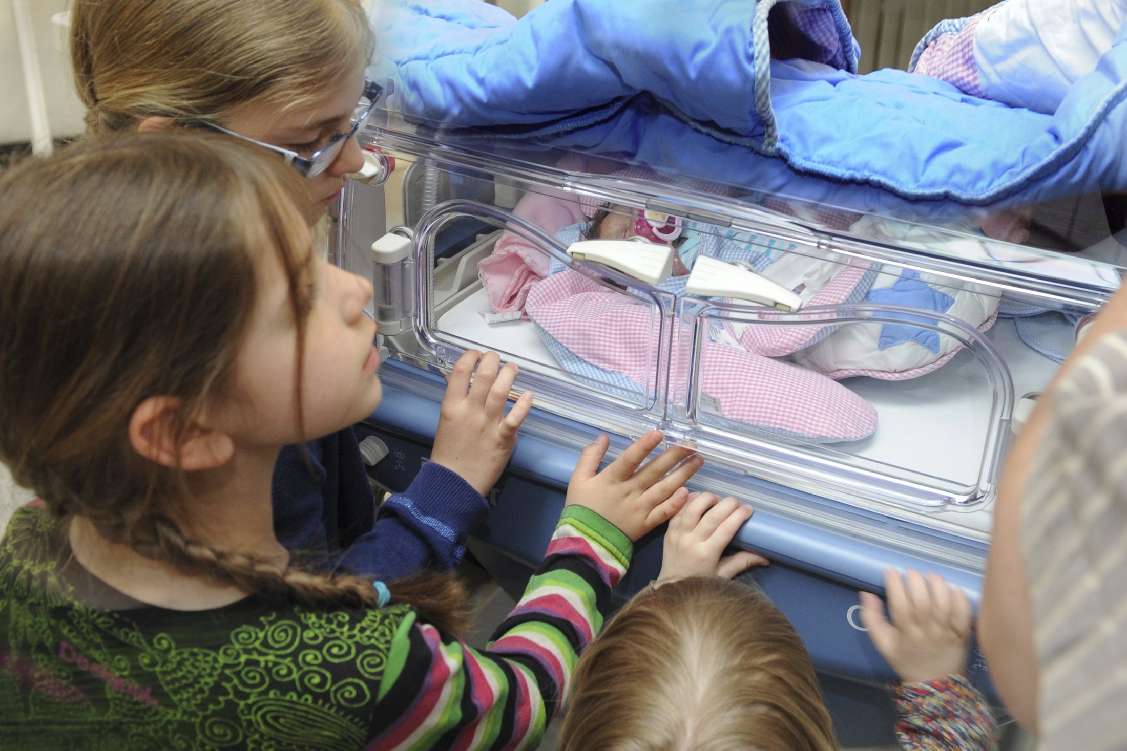 Children looking at their premature sibling in an incubator.