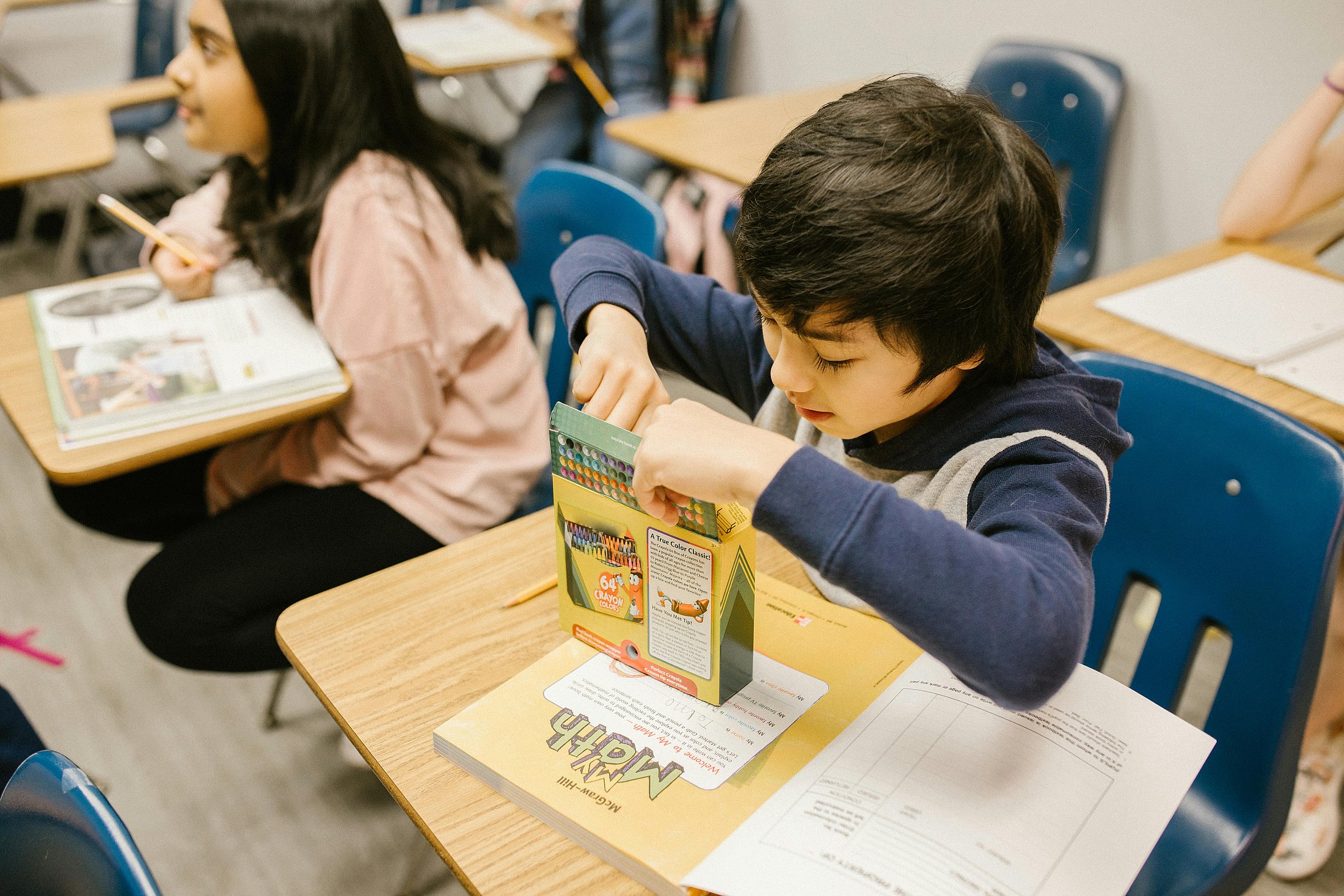 A boy opening a box of crayons during a classroom activity.