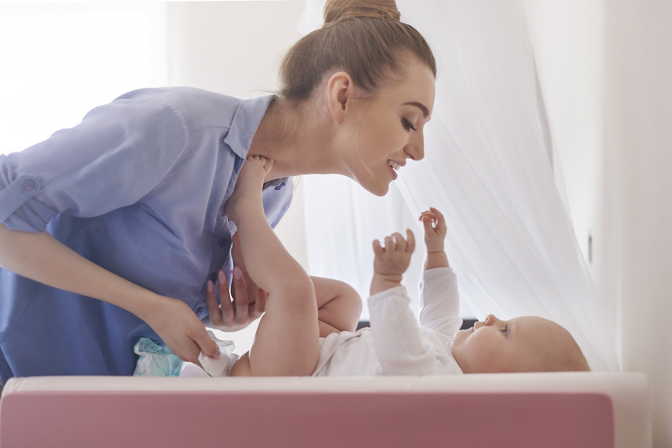 Mother changing baby’s nappy while smiling.