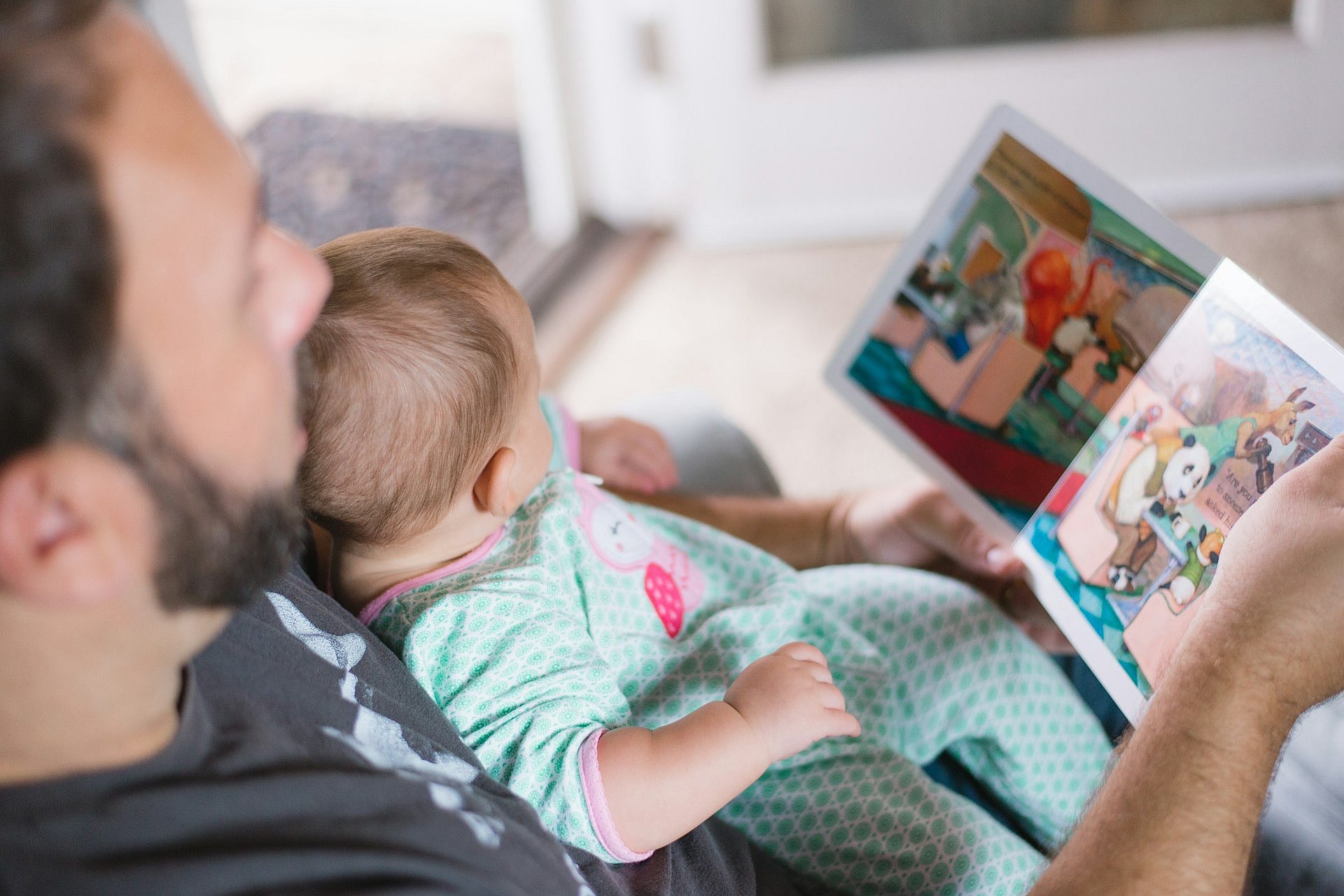 Father reading a colourful book to a baby on his lap.