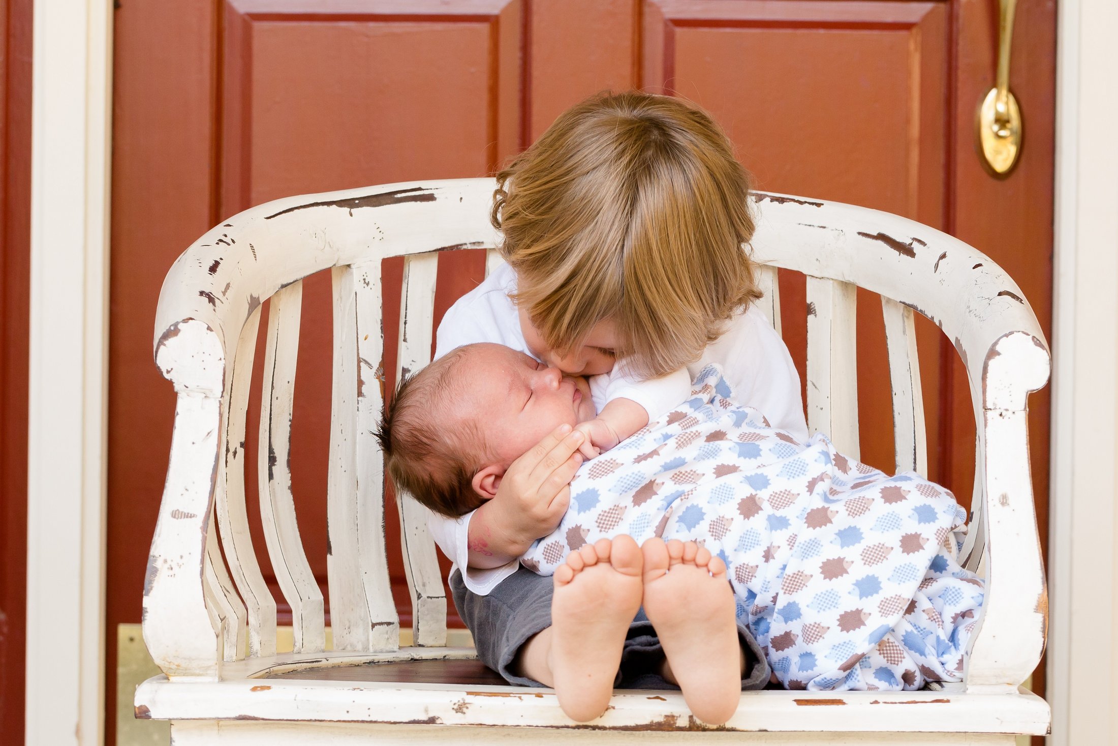Big brother kissing his premature newborn sibling tenderly.