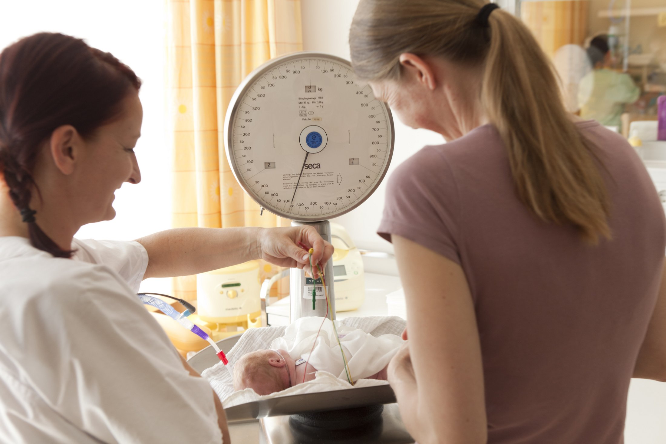 Nurse weighing a premature baby on a medical scale.