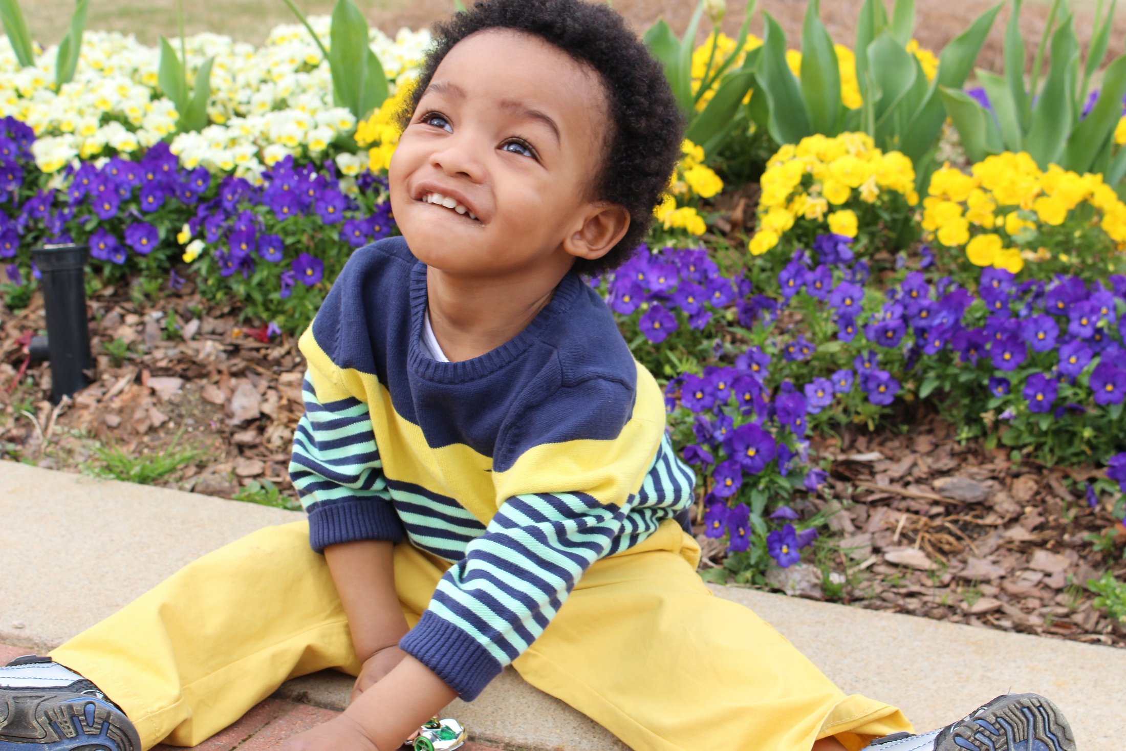 A cheerful child sitting in front of vibrant flowers in a garden.