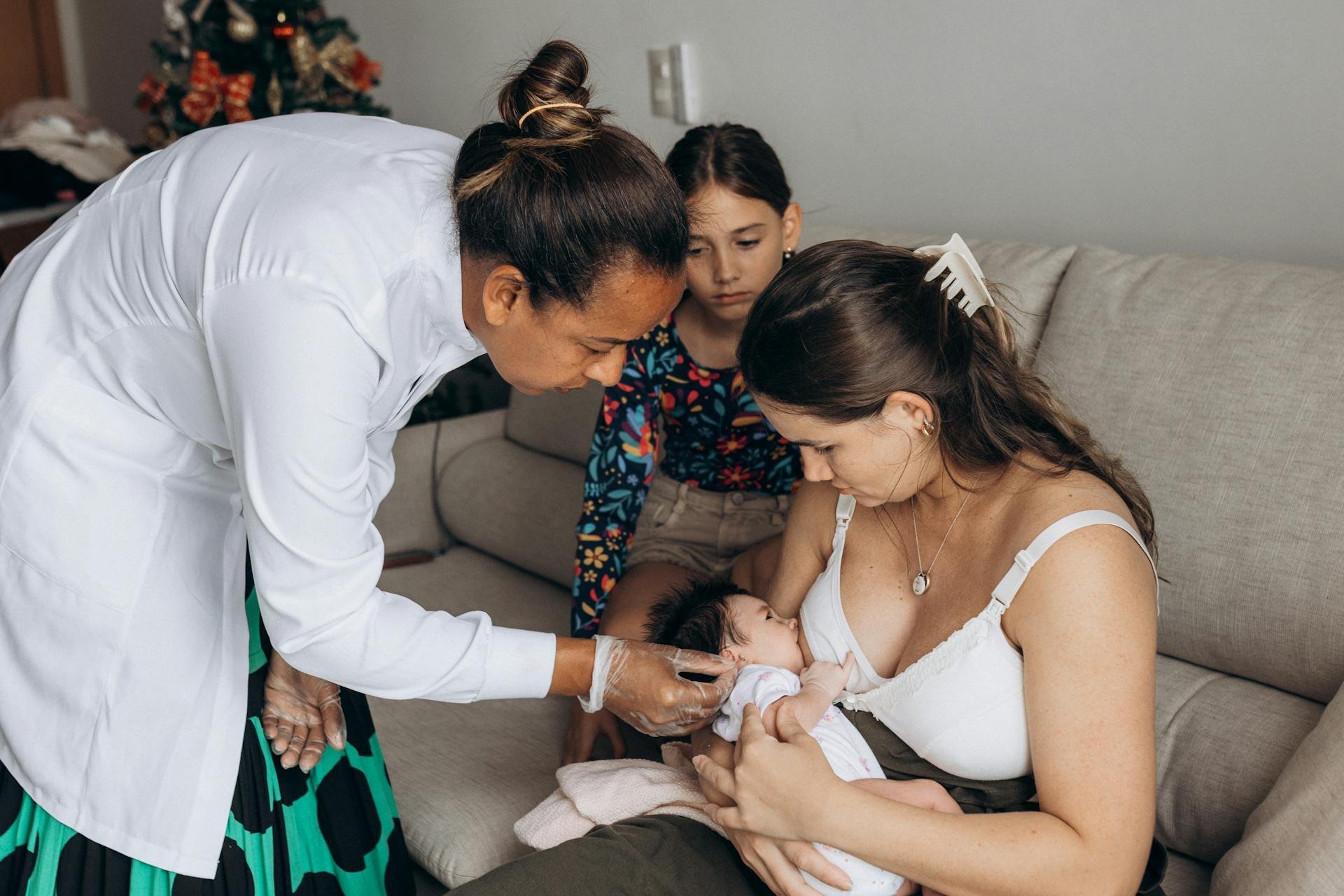 A mother breastfeeding her newborn with a healthcare professional’s guidance.