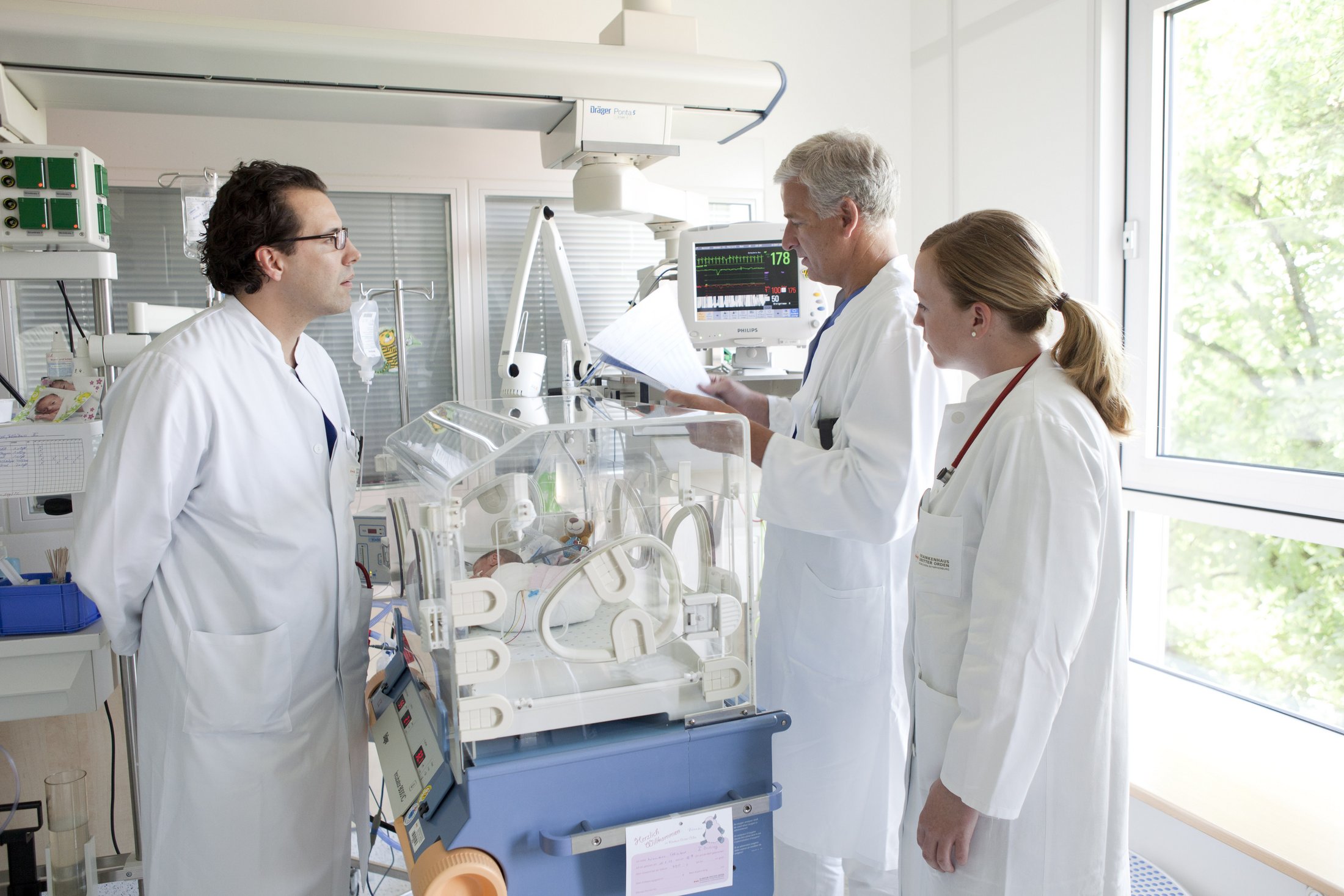 Three doctors consulting near an incubator in a NICU room.