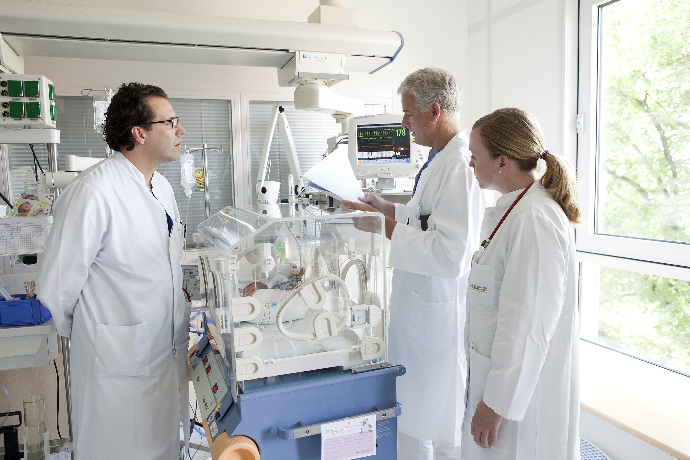 Three doctors consulting near an incubator in a NICU room.