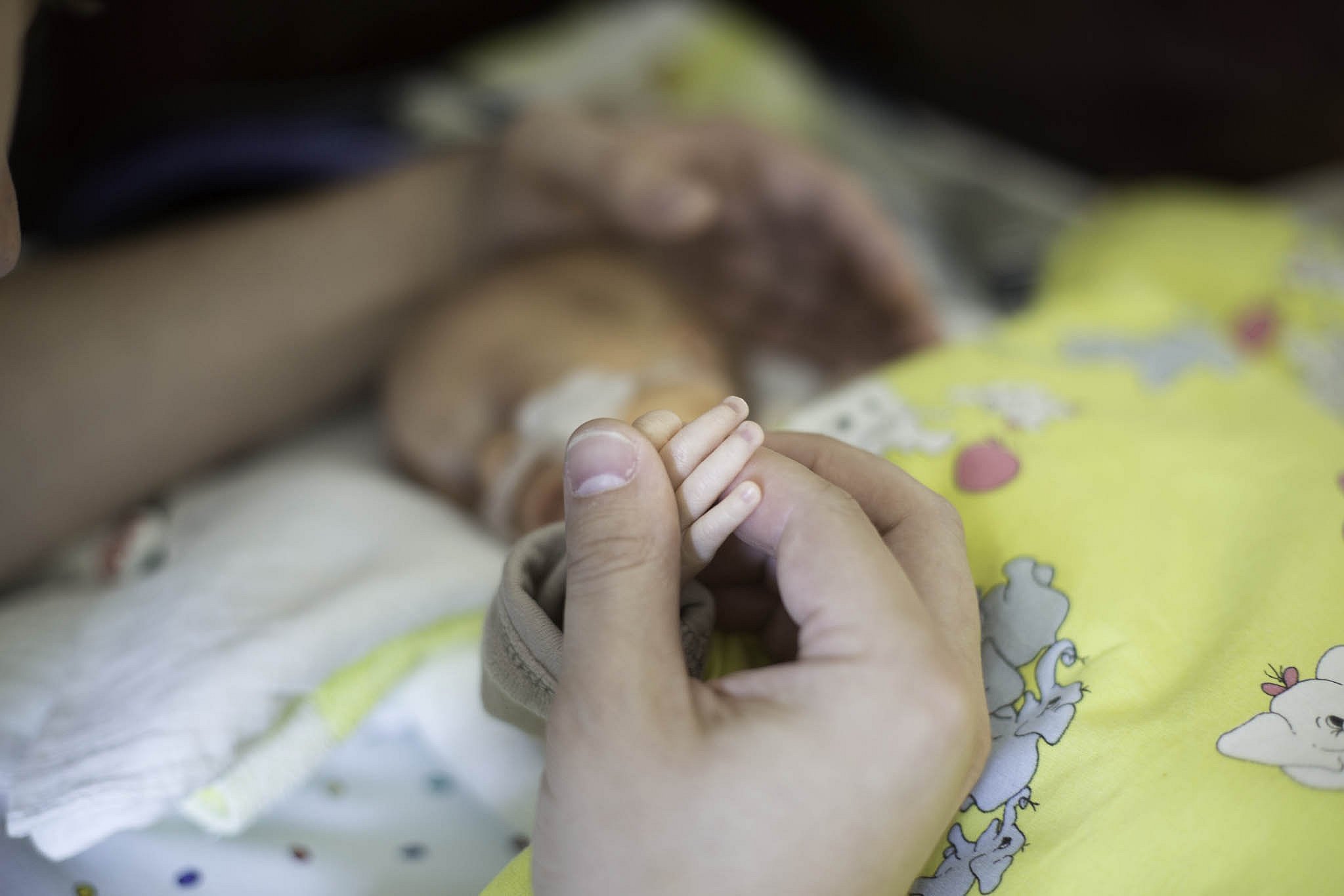 Close-up of a parent holding a premature baby’s hand.