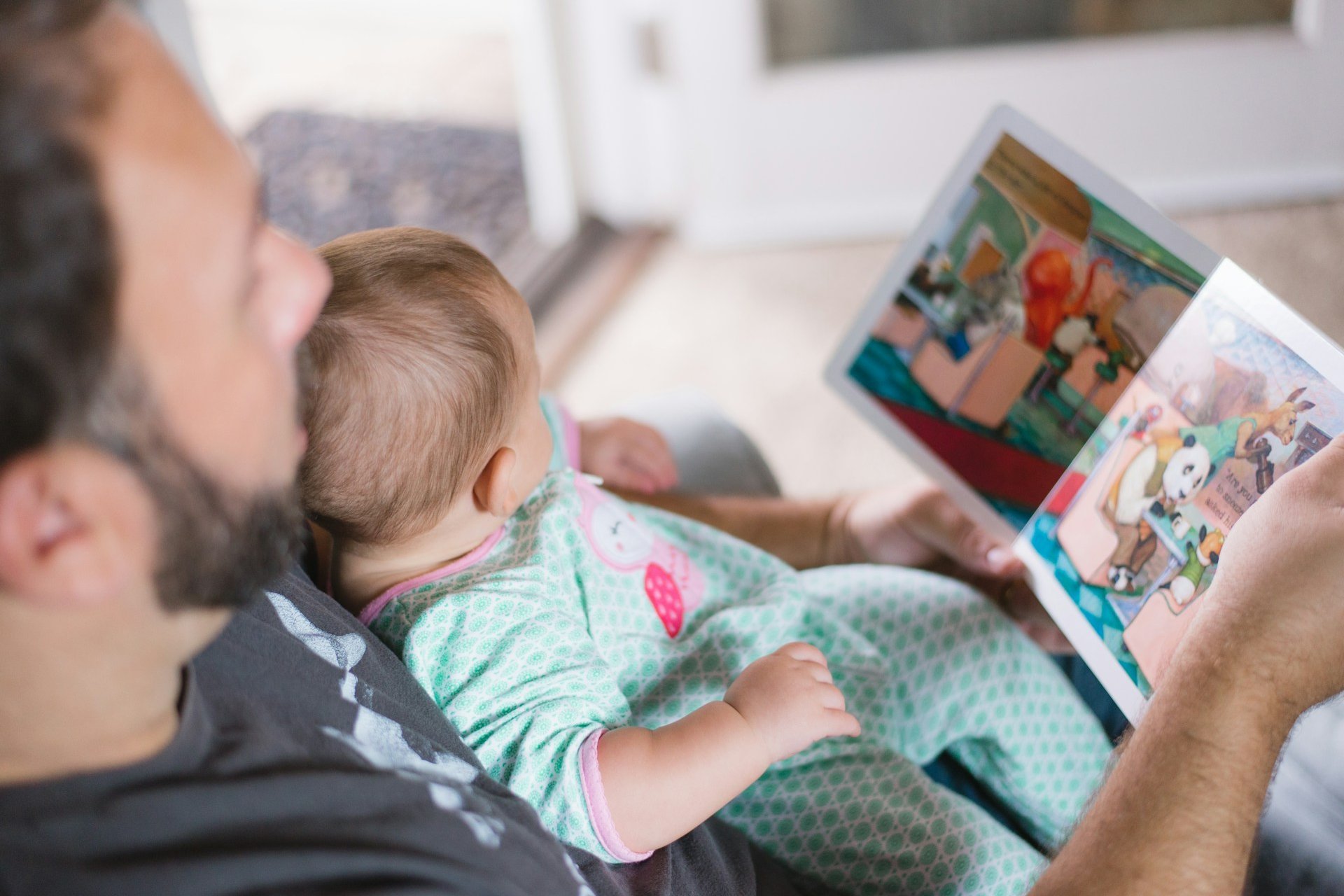Father reading a colourful book to a baby on his lap.