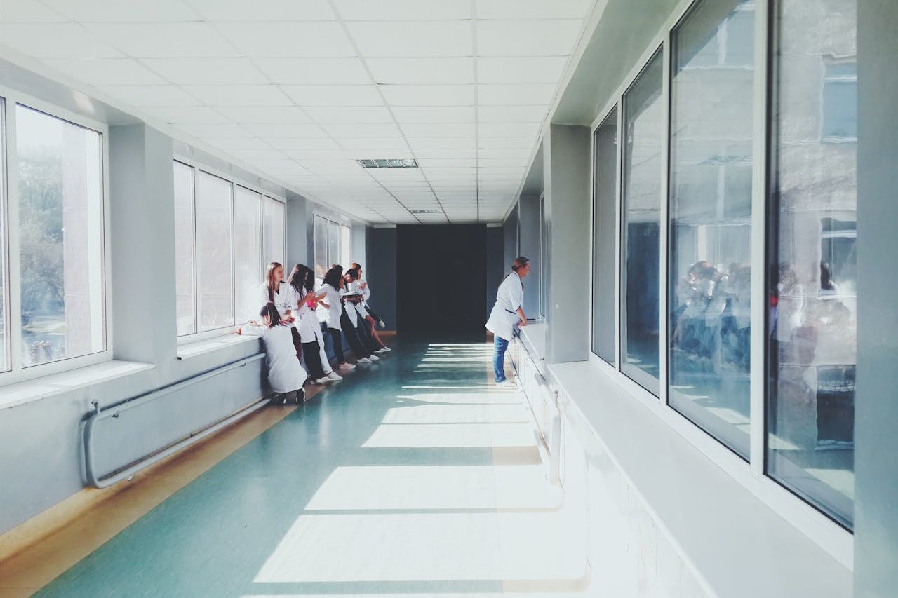Empty hospital hallway with staff gathered near windows.