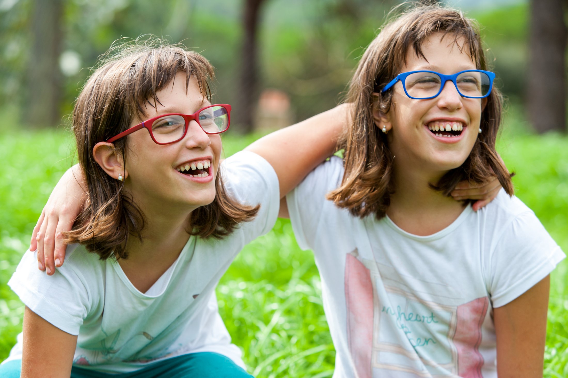 Twin girls with glasses laughing together outdoors.