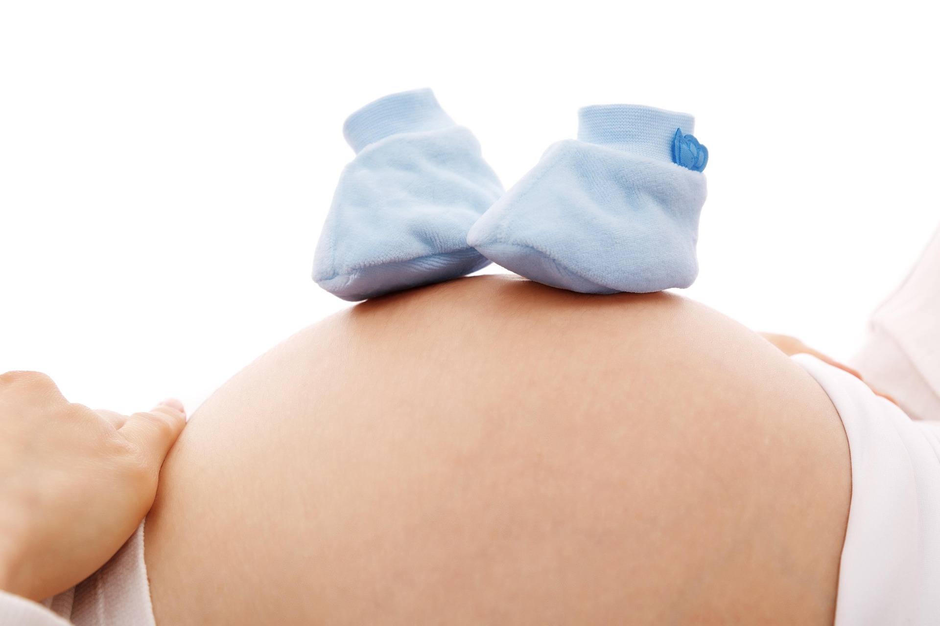 Blue baby shoes resting on a pregnant belly.