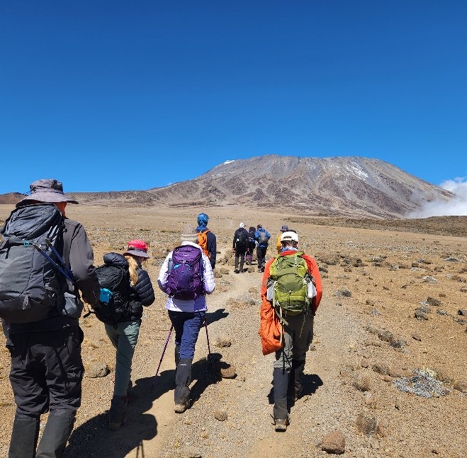 Elka, now older, seen hiking on a trail with her family towards Mount Kilimanjaro, showing her strength and progress.